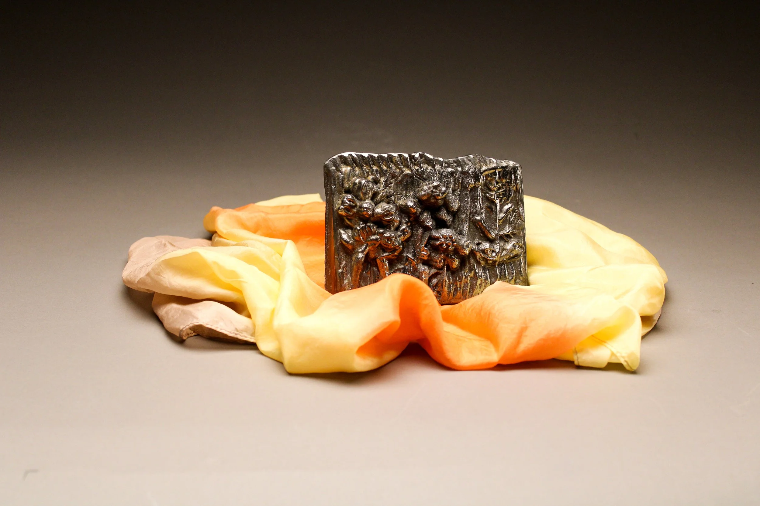 A carved black soap with intricate designs, resting on crumpled peach, pink, and yellow tissue paper.