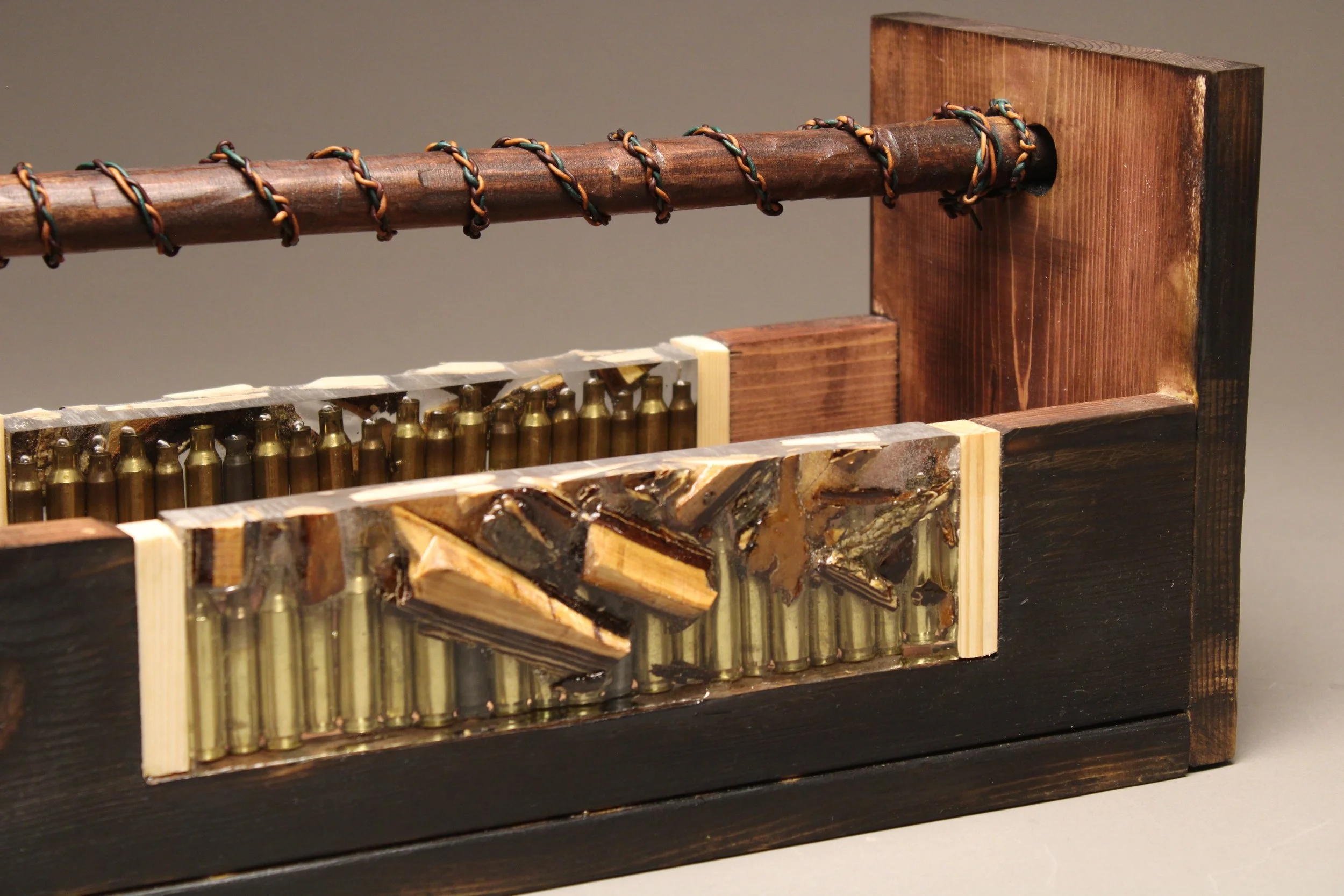 Mixed media art piece combining wood, metal, and painted elements with a wooden frame and metal bullets.