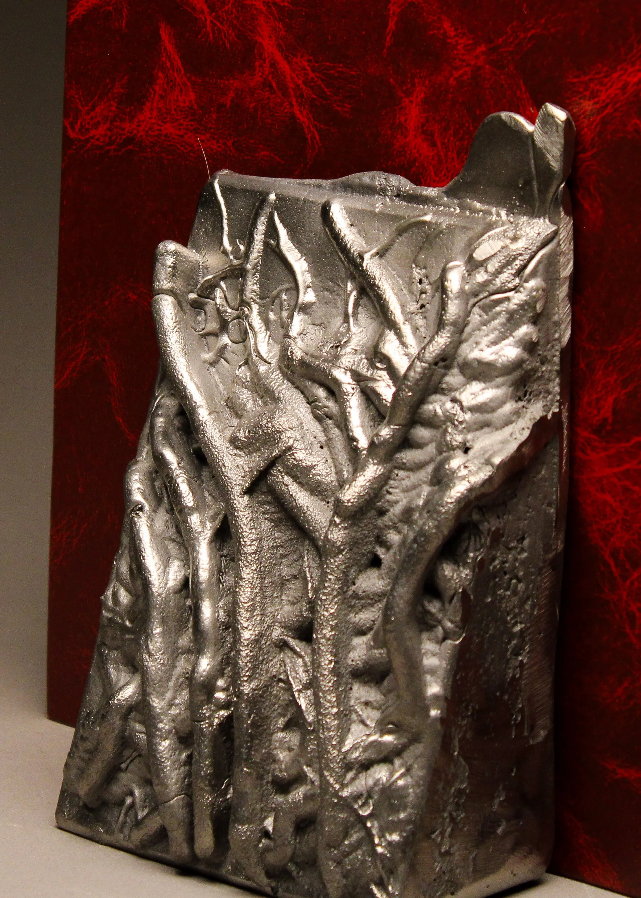 A metallic sculpture of intertwined hands with a textured surface, placed against a red cloth background.