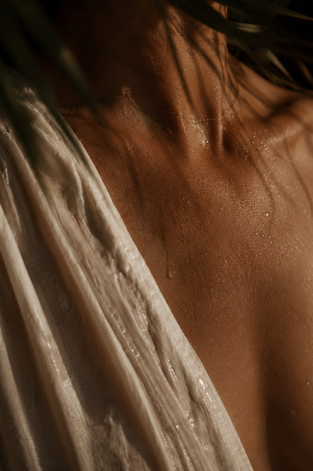 Close-up of a person's neck, shoulder, and part of their face with wet skin, wearing a light-colored, textured piece of clothing.