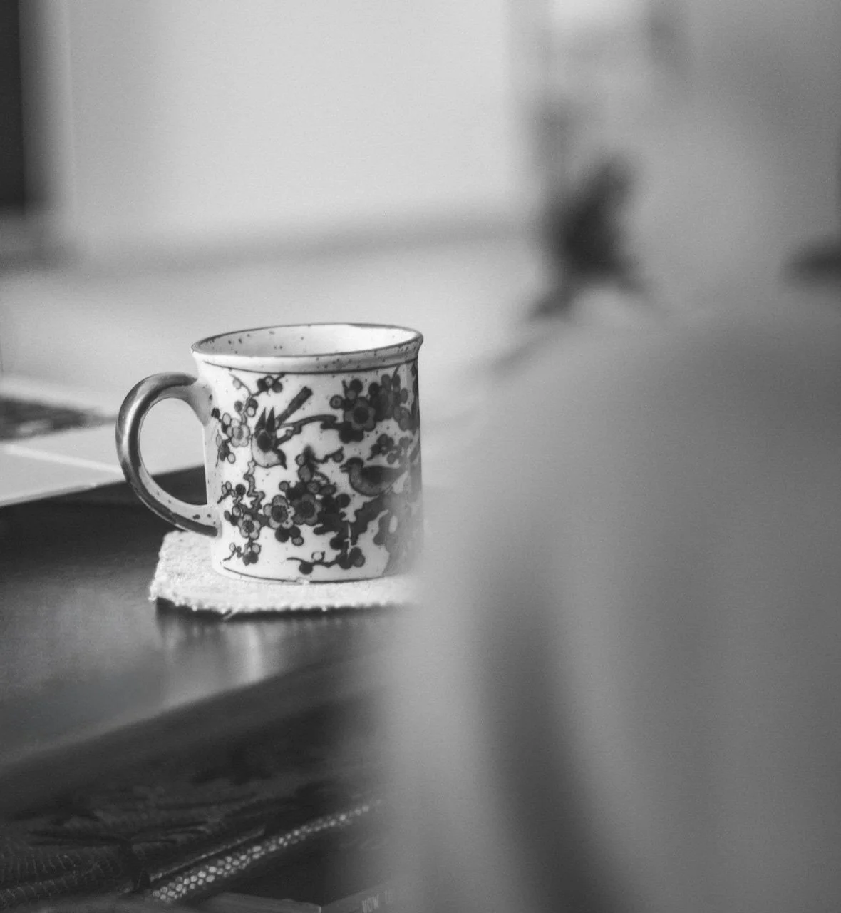 Black and white photo of a ceramic mug with floral design on a table, blurred background.