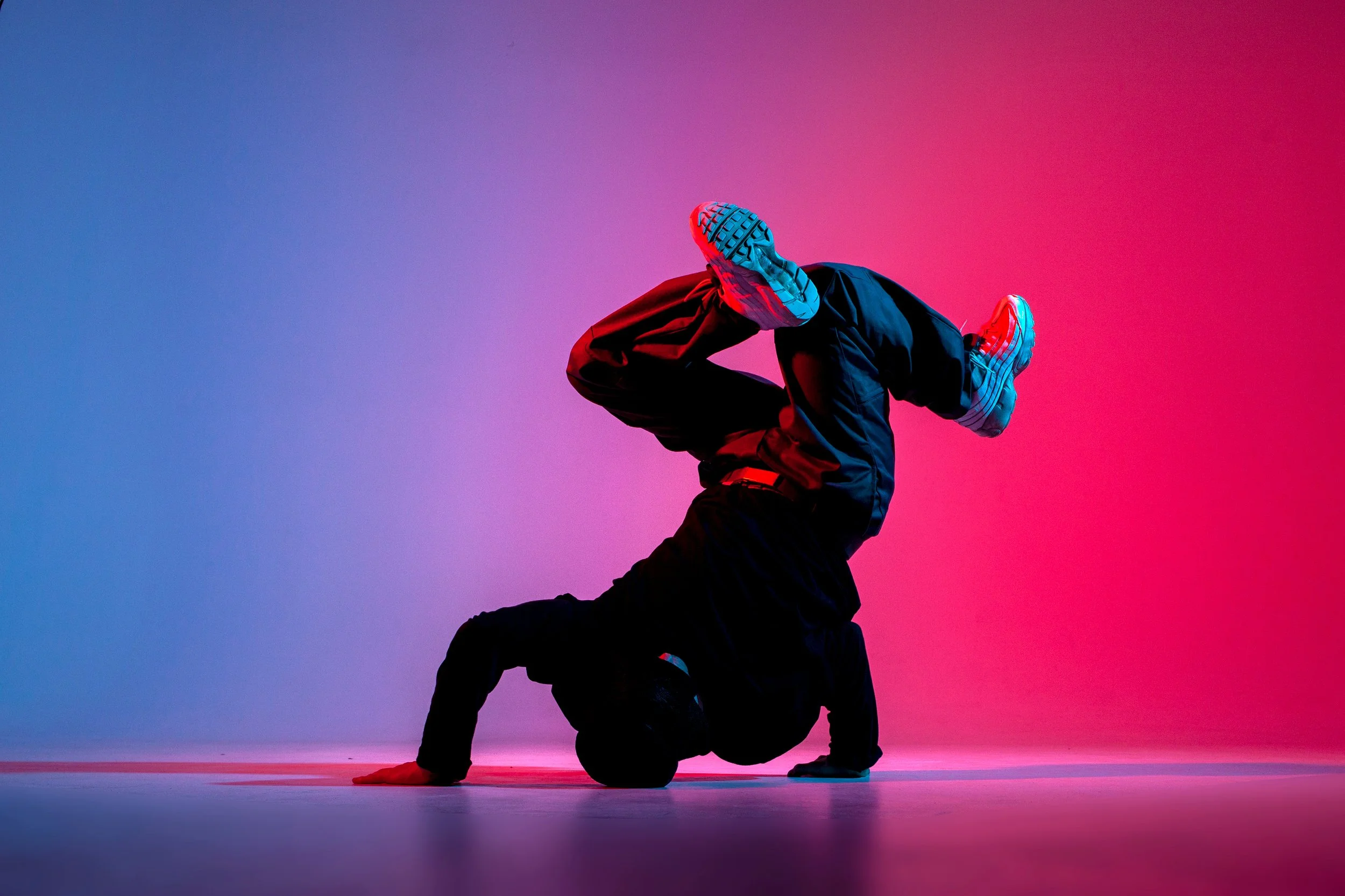 Two people performing a handstand pose with one person supporting the other, against a blue and pink gradient background.