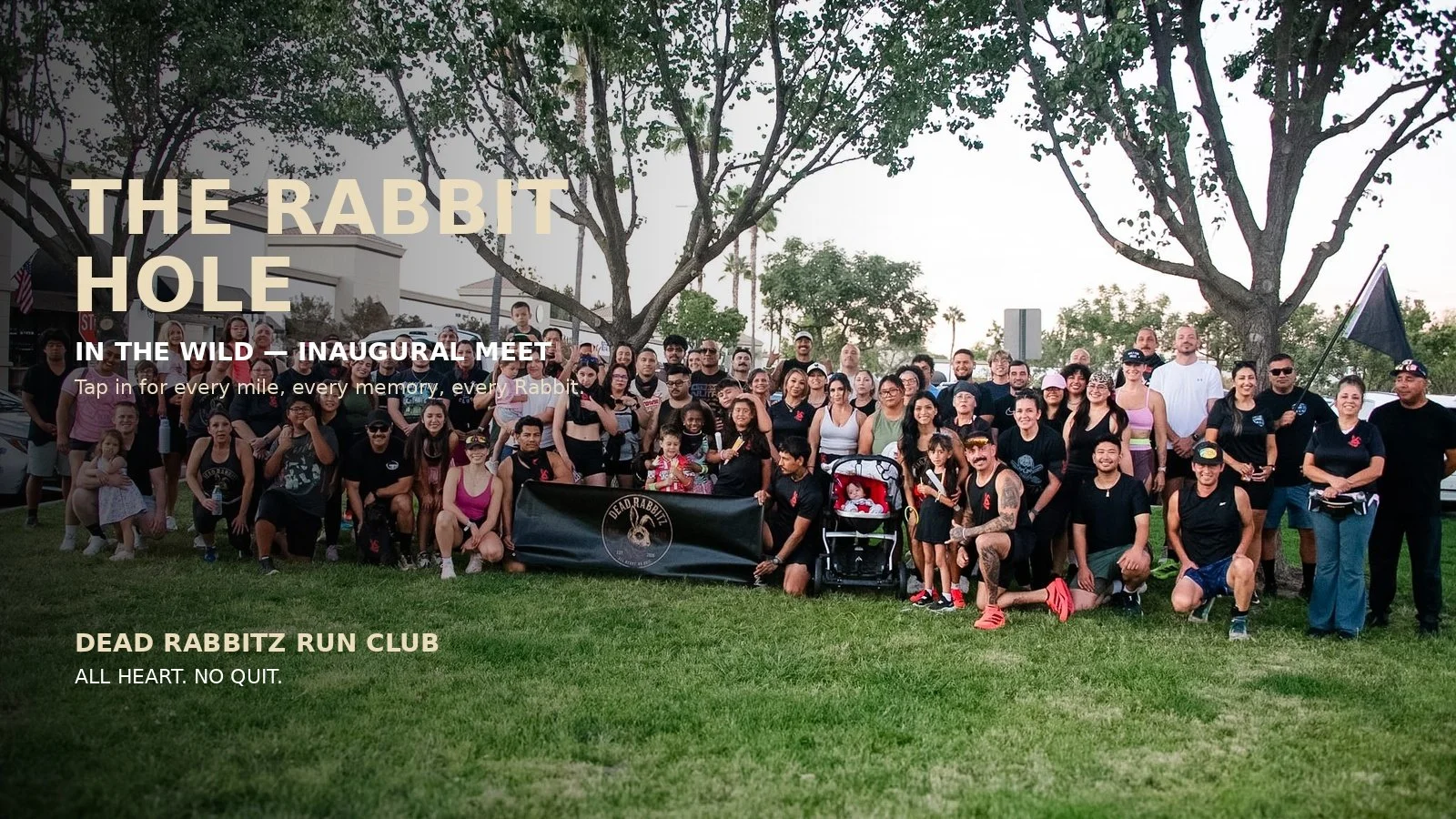 A large group of people gathered outdoors for a community event, holding a banner that reads 'Dead Rabbitz Run Club.' Trees and buildings are visible in the background, and everyone is smiling and posing for the photo.