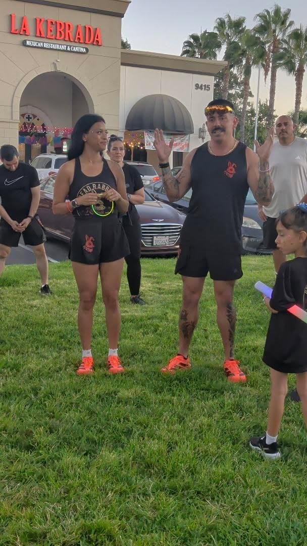 A group of people gathered outside La Kebrada Mexican Restaurant & Cantina, with palms in the background, appearing to participate in an event or activity on the grass.