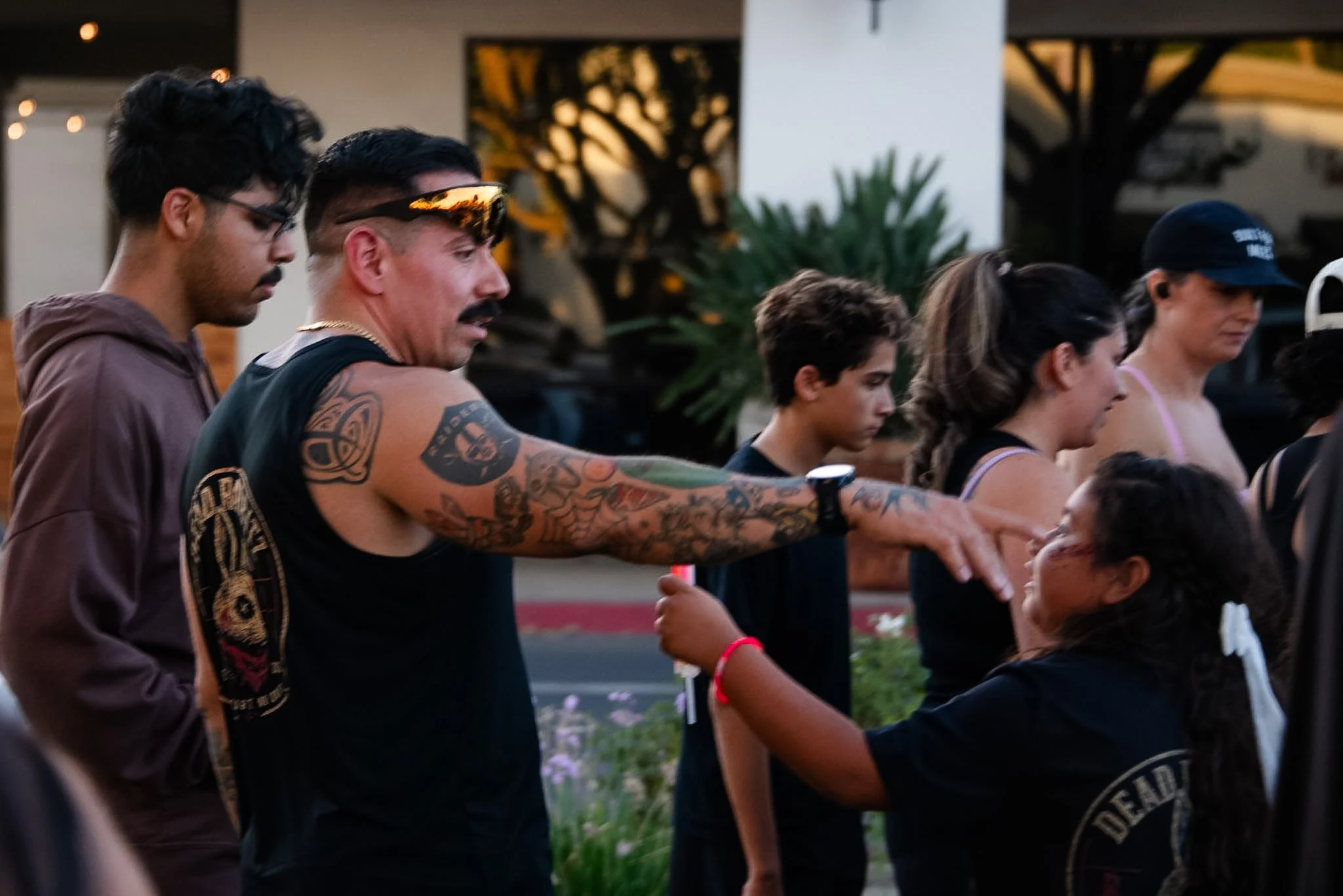 A group of diverse people standing in a line outdoors during sunset, with some placing their hands on the shoulders of those in front, engaged in a prayer or moment of reflection.