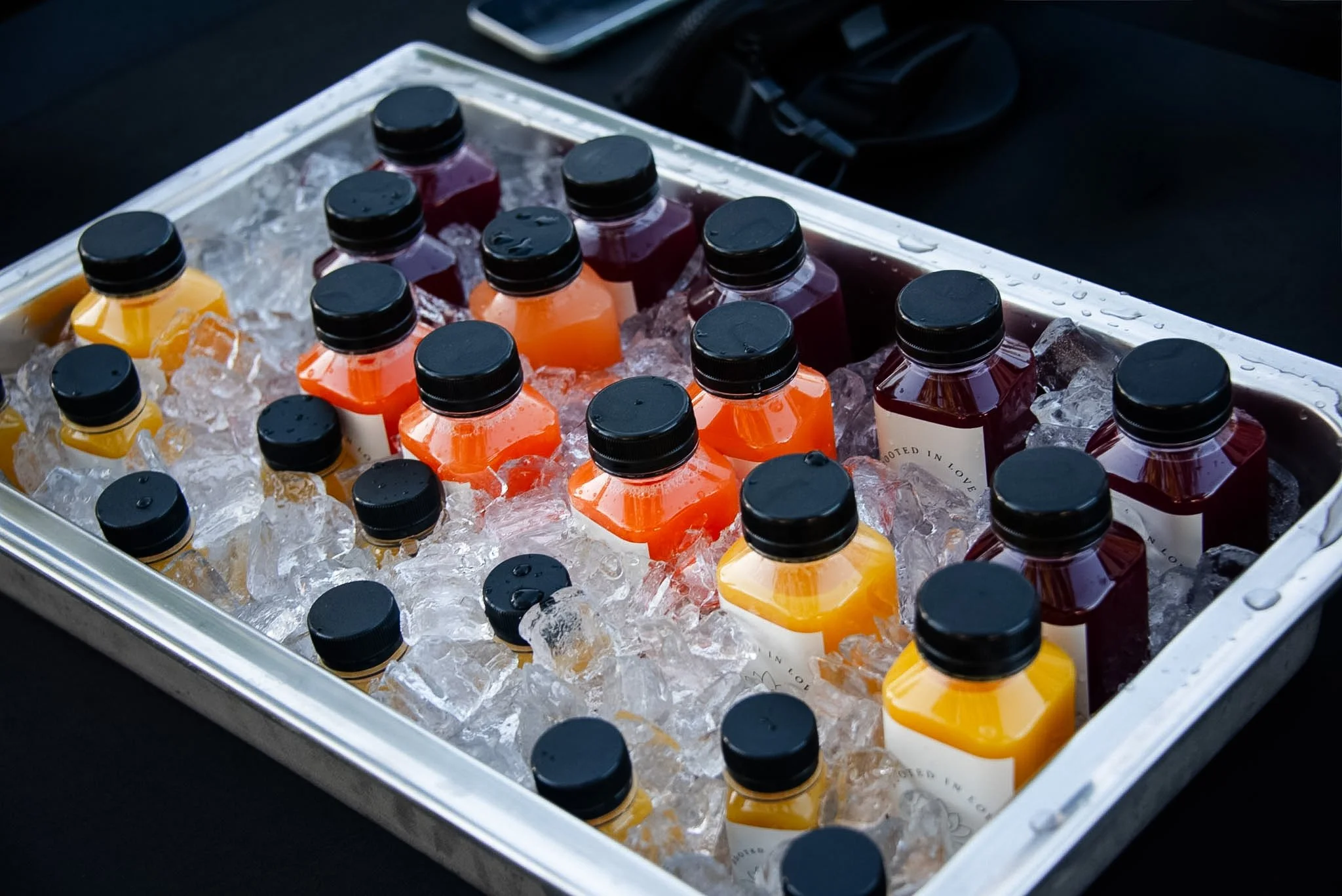 Bottles of colorful beverages on ice in a metal container.