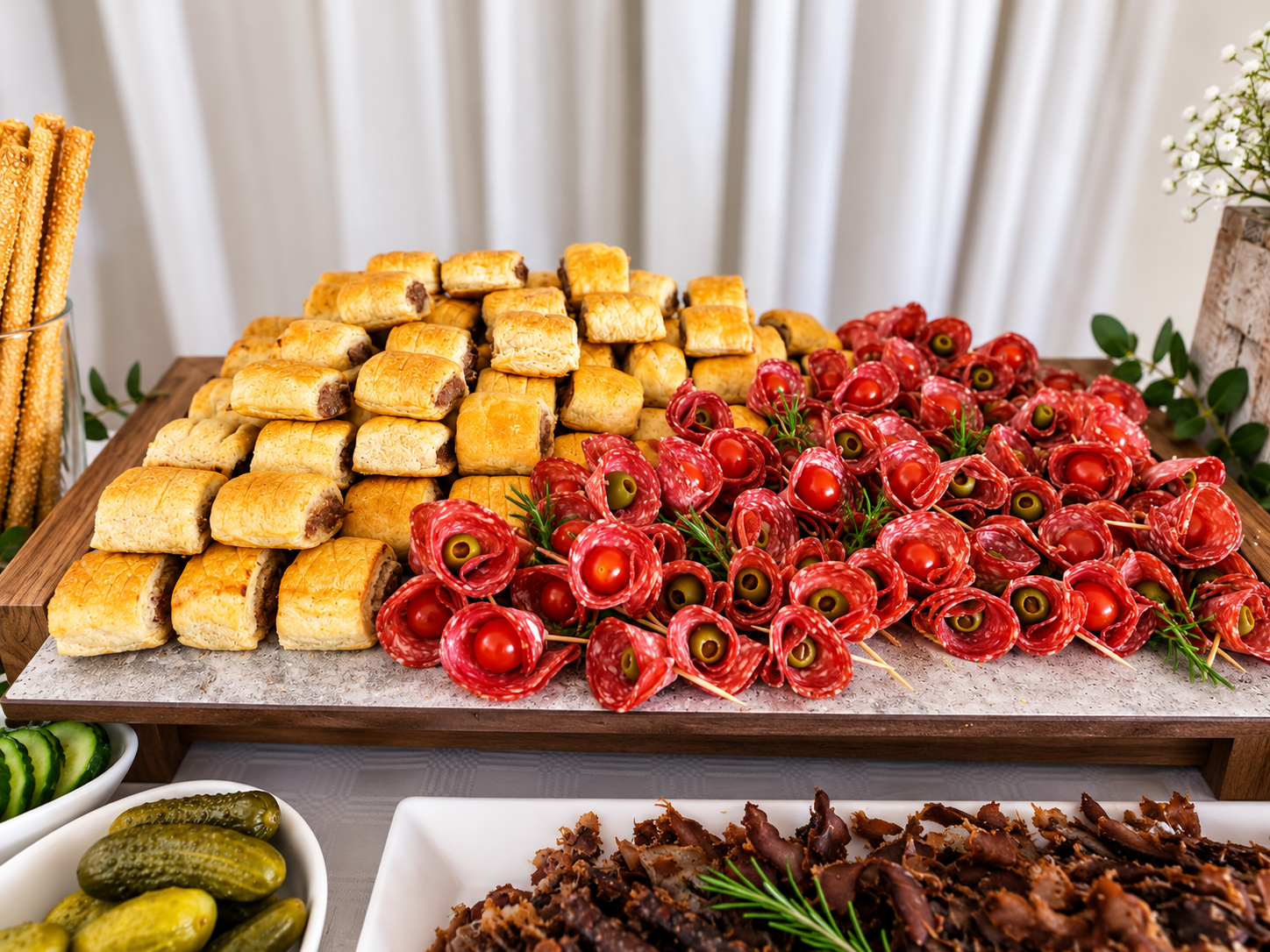 Assorted appetizer platter featuring small pastry squares and red meat and olive appetizers decorated with sprigs of herbs.