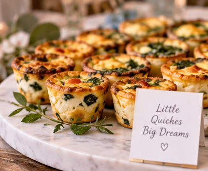 A marble serving tray with baked mini quiches topped with herbs, accompanied by a card that reads "Little Quiches Big Dreams" with a heart symbol.