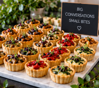 Assorted fruit tarts with berries and small desserts on a marble tray, with a blackboard sign reading 'Big Conversations Small Bites'