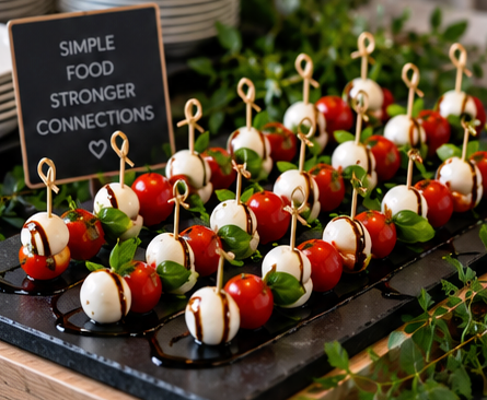 Caprese skewers with cherry tomatoes, mozzarella balls, basil, and balsamic drizzle on a black platter.