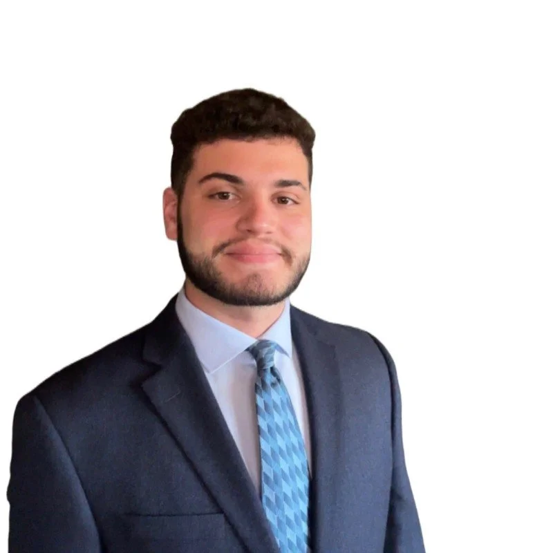 A young man in a business suit with a blue tie standing against a white background.