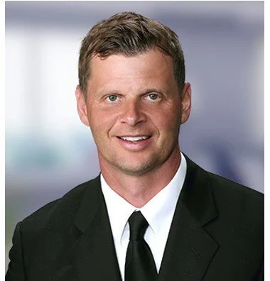 Professional headshot of a man in a suit and tie, smiling.