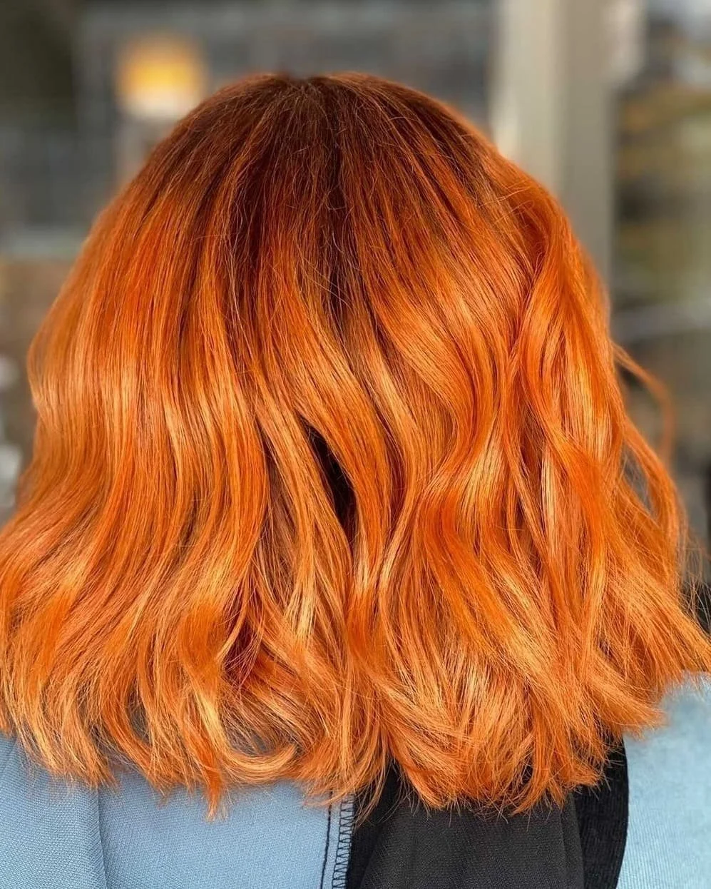 Back view of a woman with shoulder-length wavy hair dyed in a vibrant orange shade.