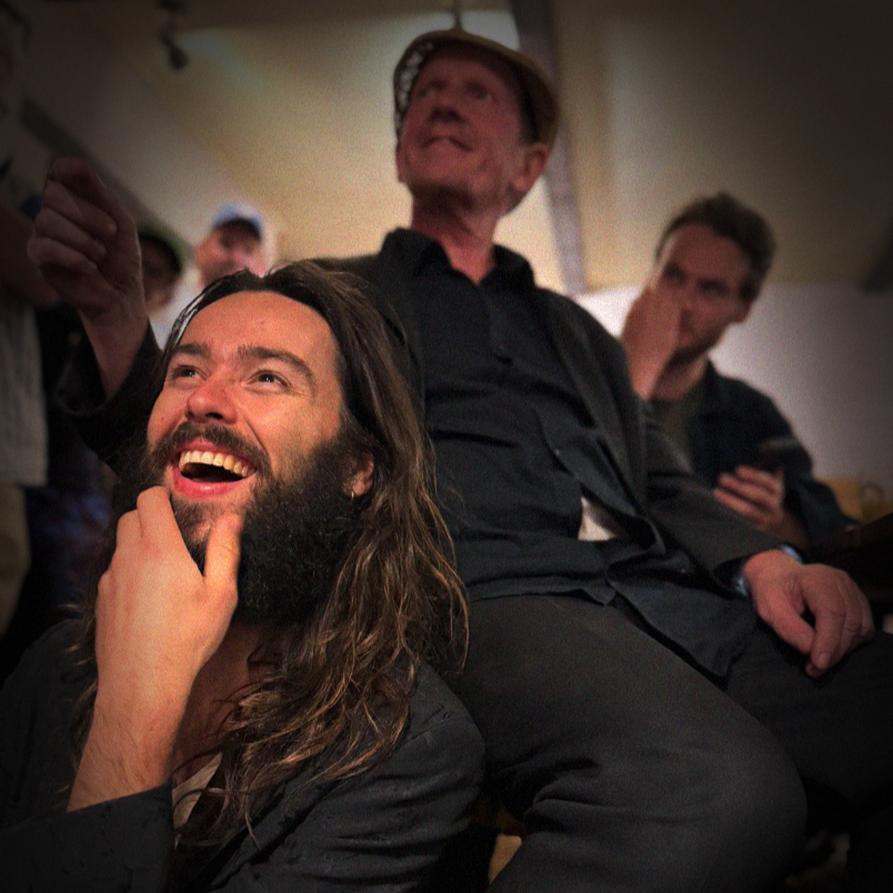 Three men enjoying an event, with two in the foreground smiling and a third man in the background looking on.