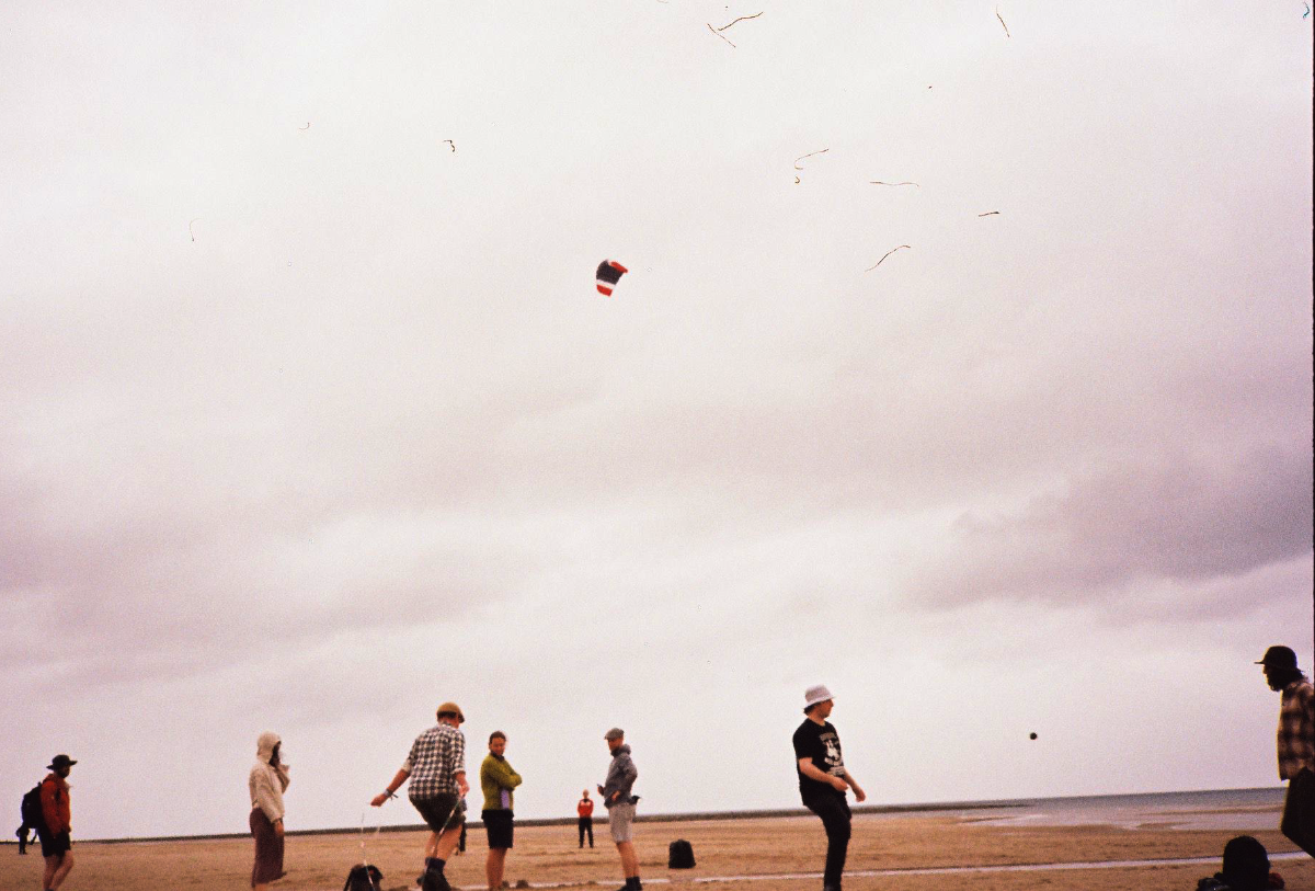Group of people on a beach flying a kite in a cloudy sky.