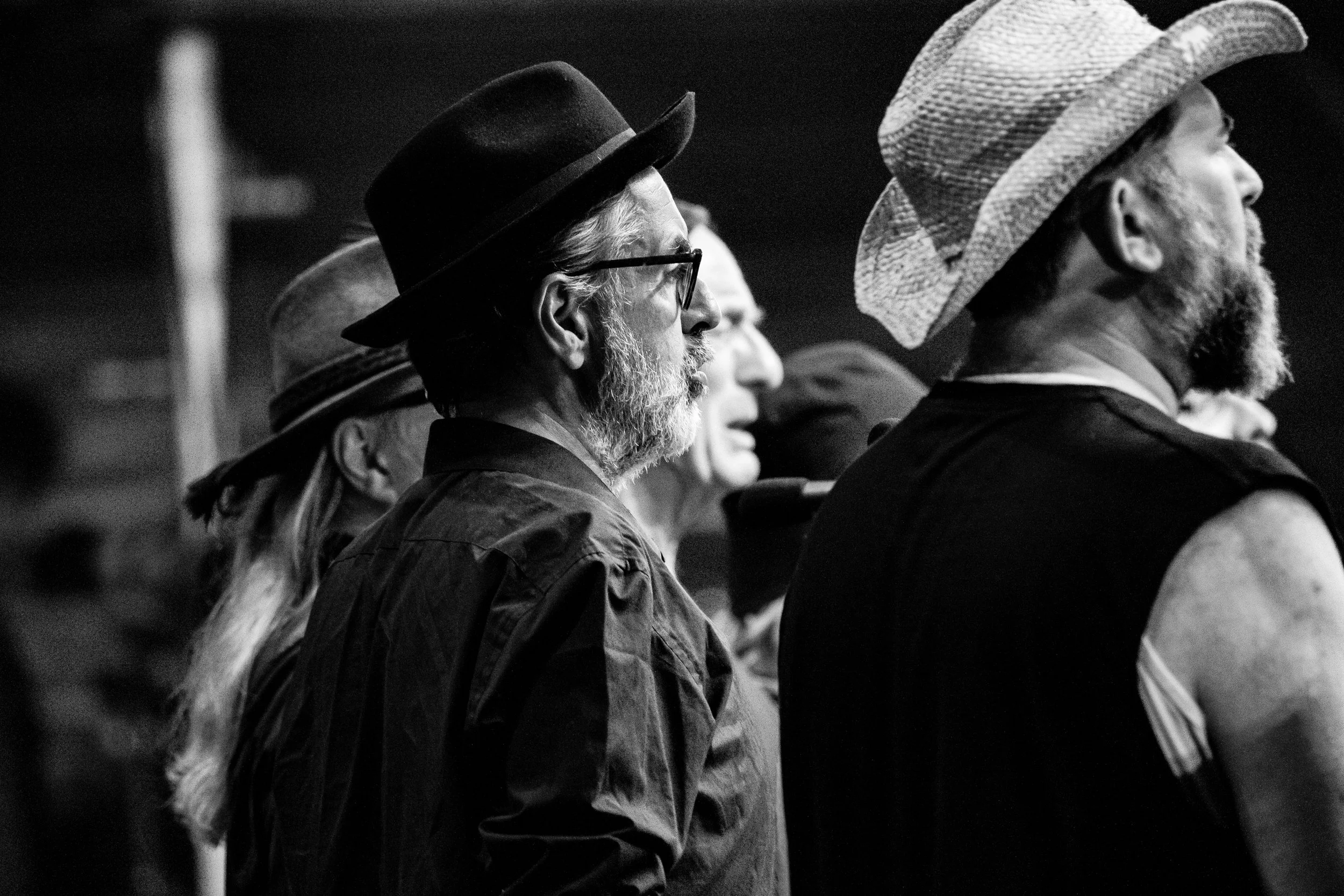 Three elderly men with gray hair and beards, wearing hats, standing in a row at a cultural event or gathering, shown in black and white.