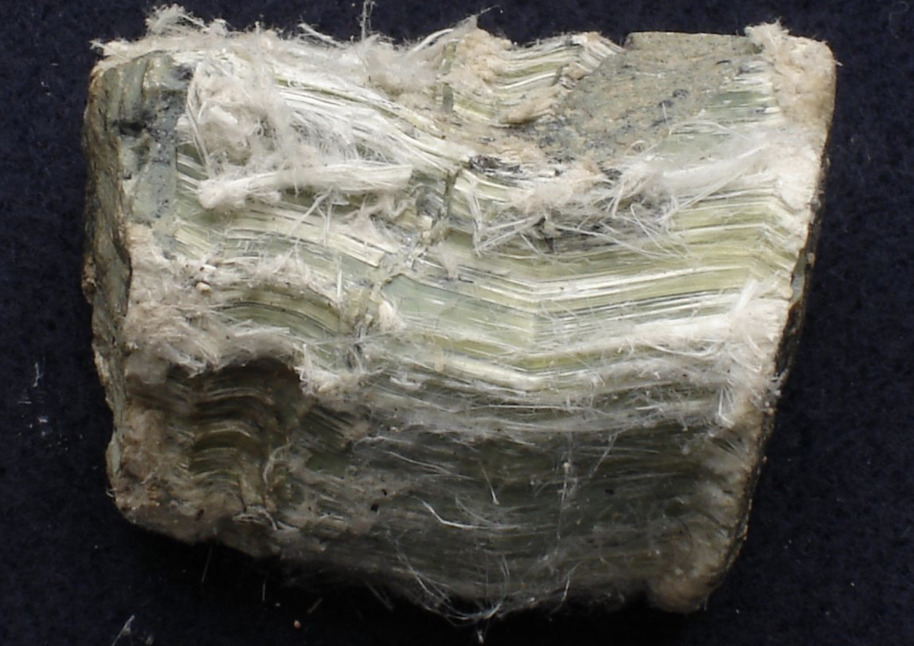 Close-up of a rough, unpolished mineral or rock with layered, fibrous appearance and pale green and white streaks.
