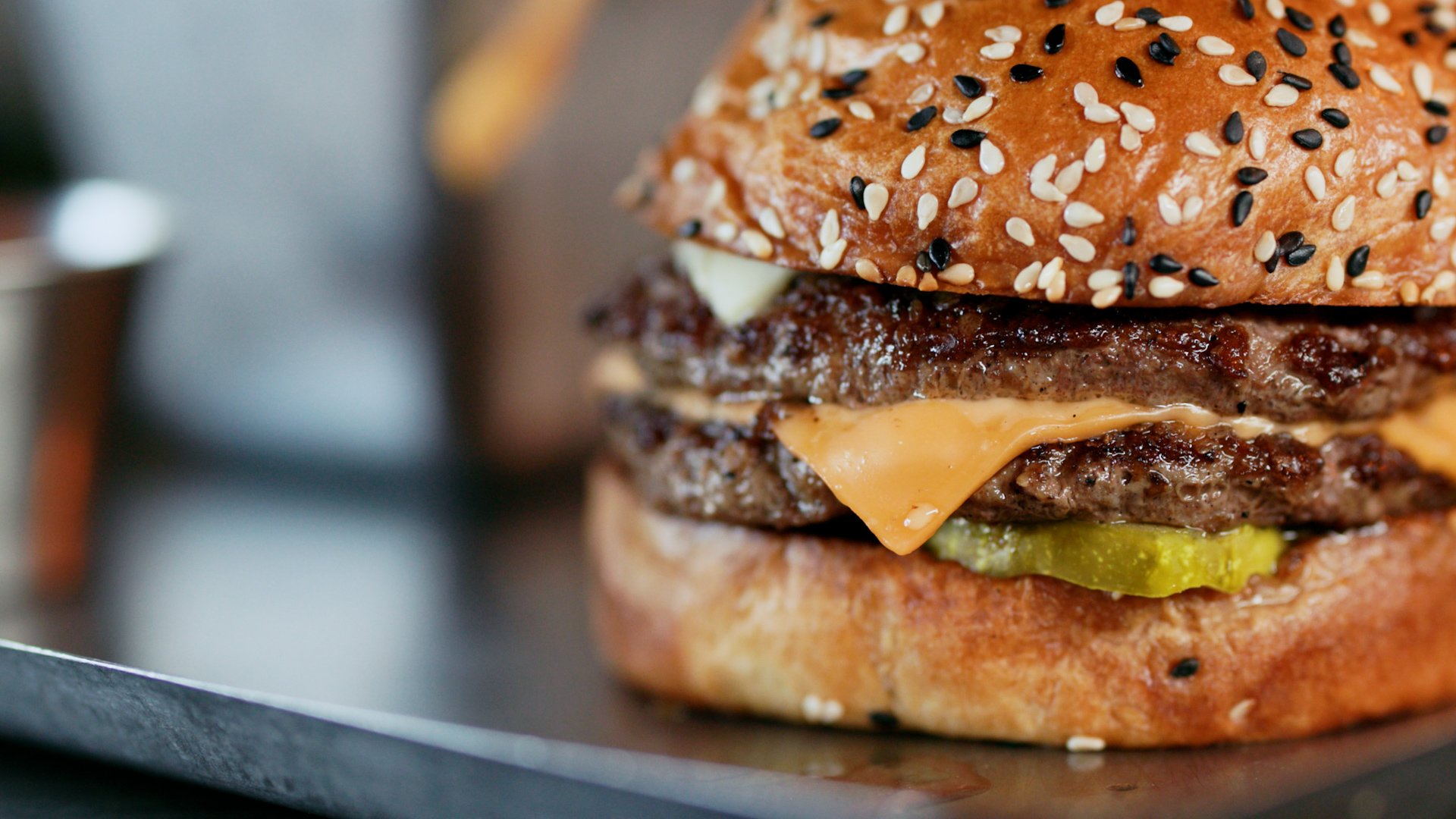 Close-up of a cheeseburger with sesame seed bun, lettuce, pickles, cheddar cheese, a beef patty, and a top bun with sesame seeds.