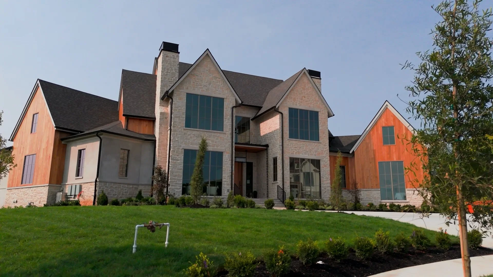 Modern house with stone and wood exterior, large windows, and a manicured front lawn.