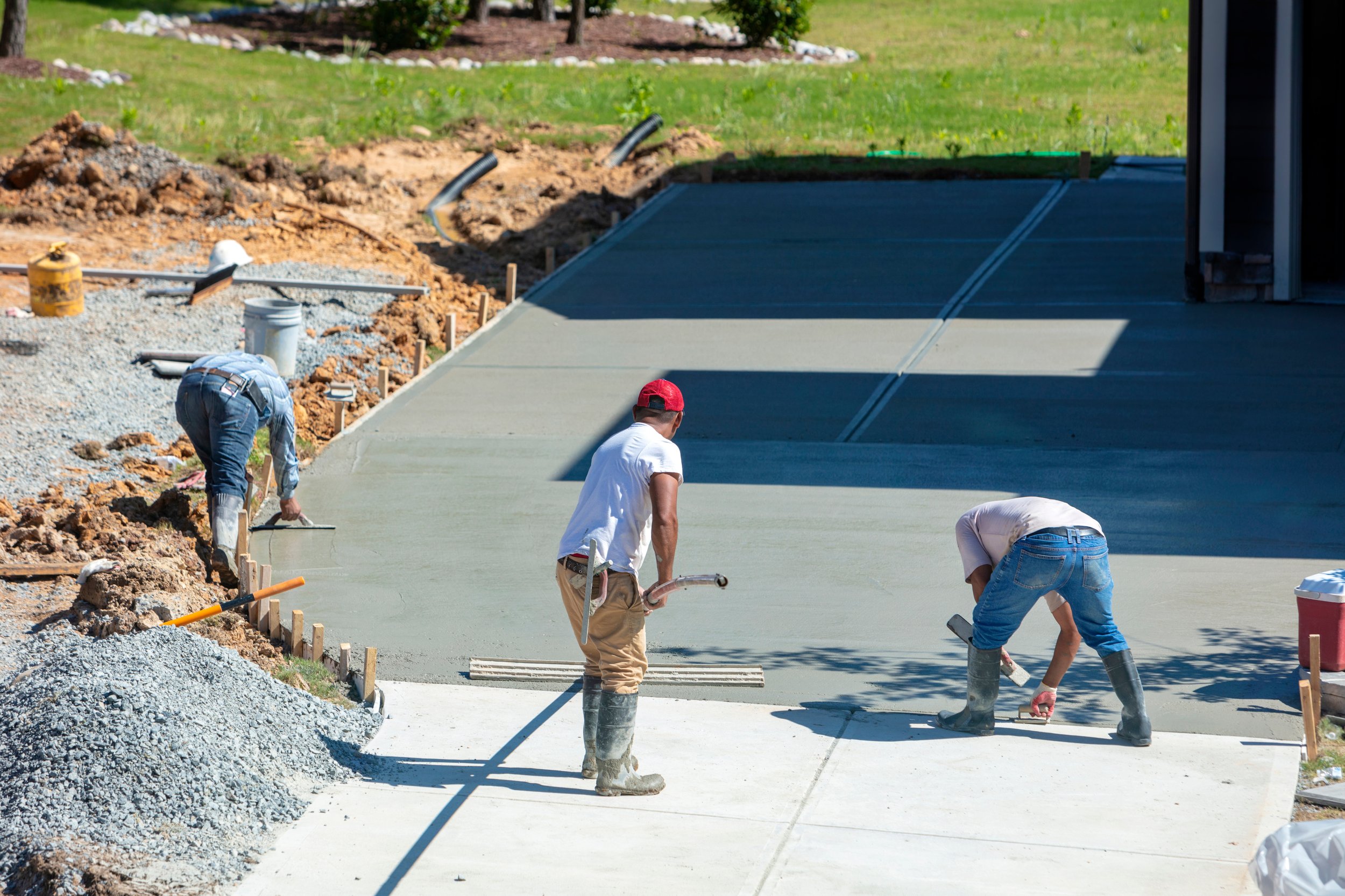 Workers pouring and spreading concrete on a driveway during construction on a sunny day.