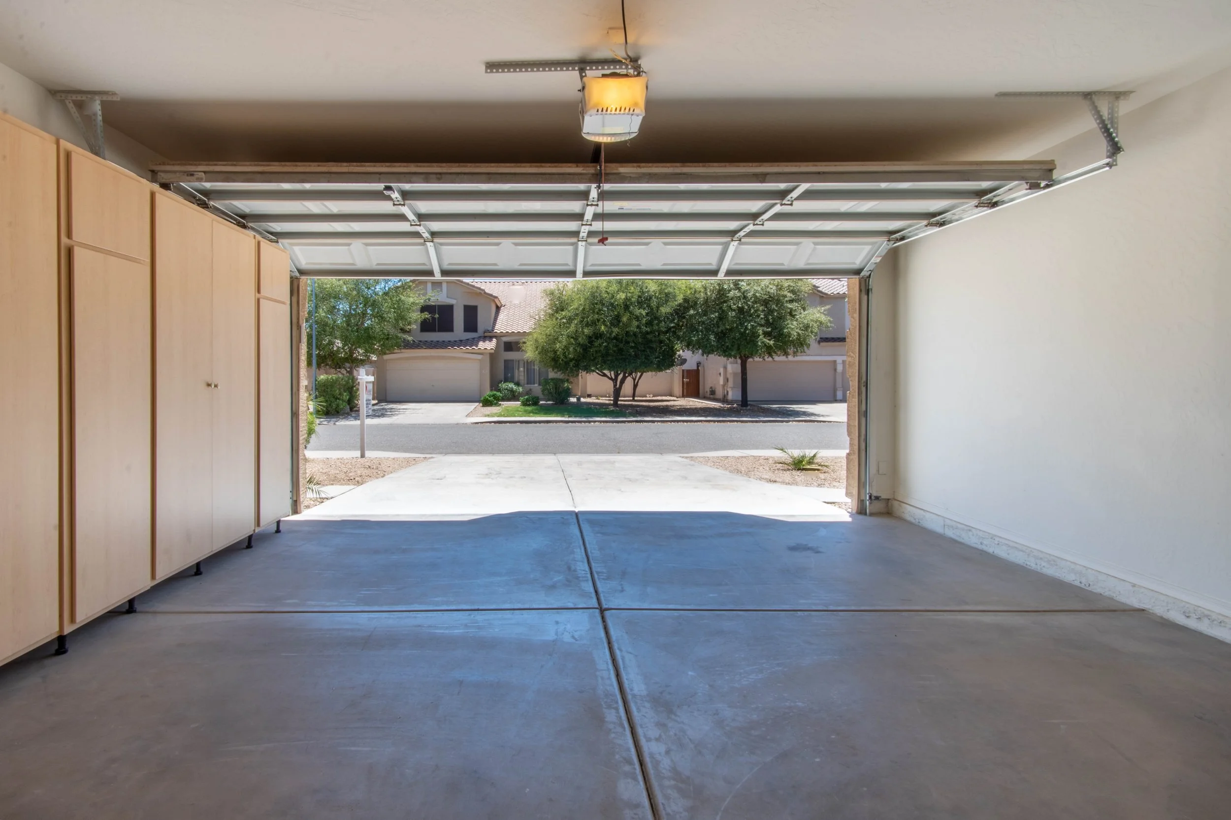 View from inside a garage looking outside at a suburban street with trees and houses.