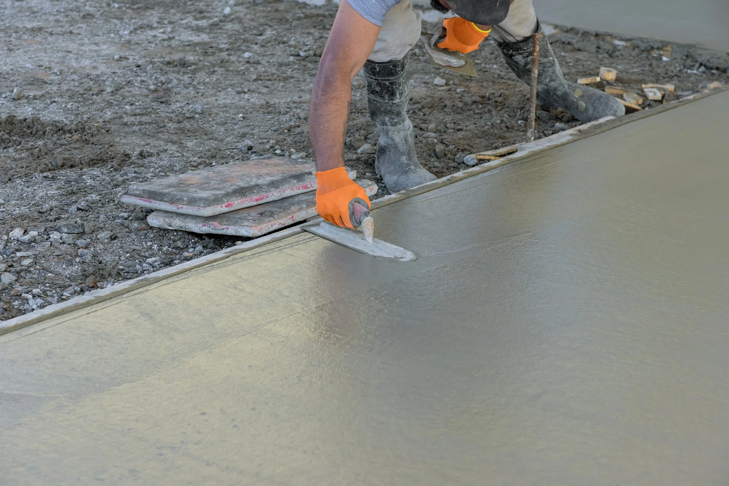 Construction worker using a trowel to smooth wet concrete on a sidewalk or pavement.
