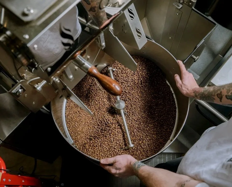 Person operating a coffee roasting machine filled with roasted coffee beans.