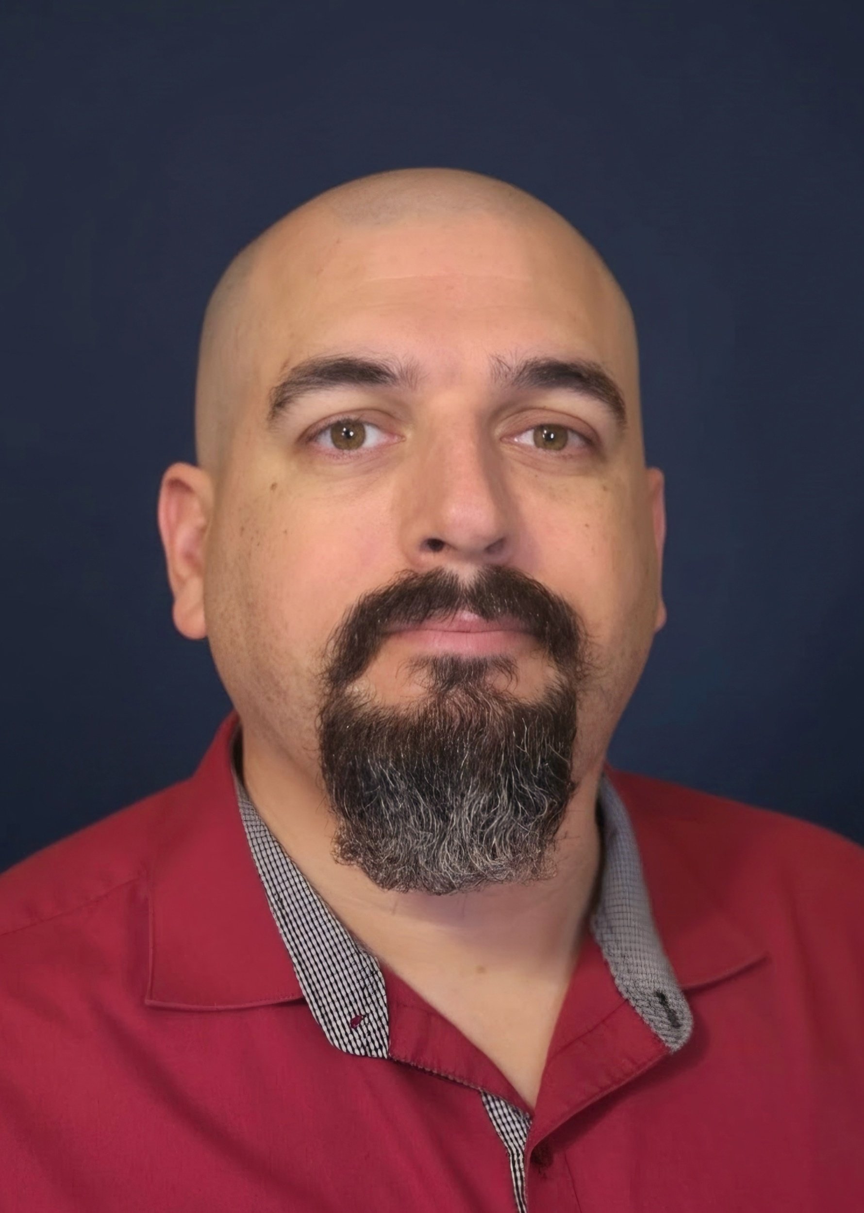 Close-up of a man that is the site owner, with a salt and pepper mustache and goatee, wearing a red button up with the collar open at the neck, against a dark blue background.