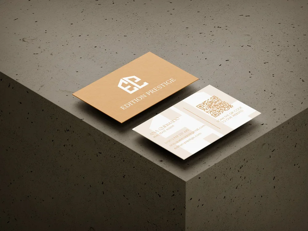 Cartes de visite pour promoteur immobilier, avec logo, coordonnées et code QR, posées sur une surface en béton.