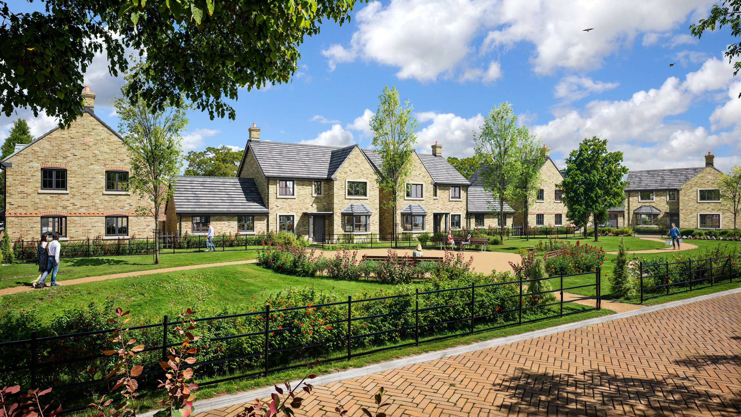 A peaceful residential community with two-story brick houses, a well-maintained grassy park, walking paths, benches, and people strolling and sitting, under a bright blue sky with scattered clouds.