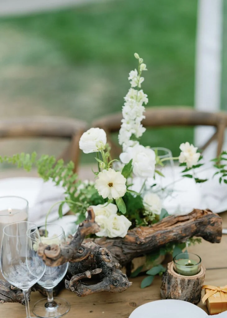 White floral centerpiece with driftwood and ferns offering natural, elegant wedding design ideas for tables.