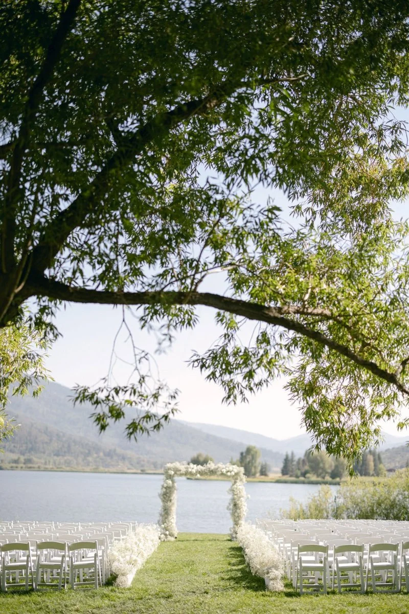 Lakeside wedding ceremony with white floral arch and mountain views, designed by a full-service wedding planner.