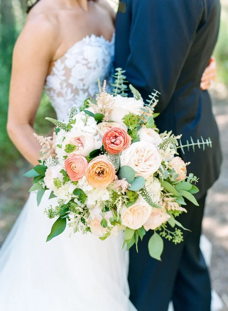 Bride and groom embrace outdoors during a Wedding at The Mount, with the bride holding a lush bouquet of garden roses, ranunculus, and greenery.