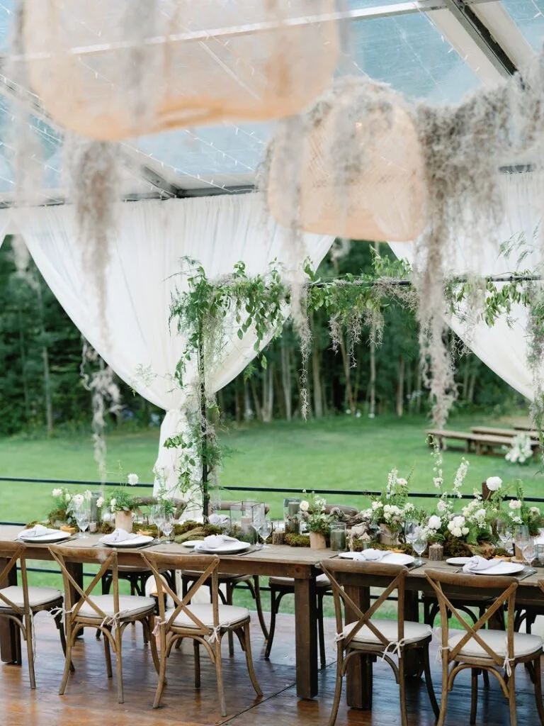 Reception setup with rustic tables, hanging moss, and greenery reflecting organic wedding design ideas.