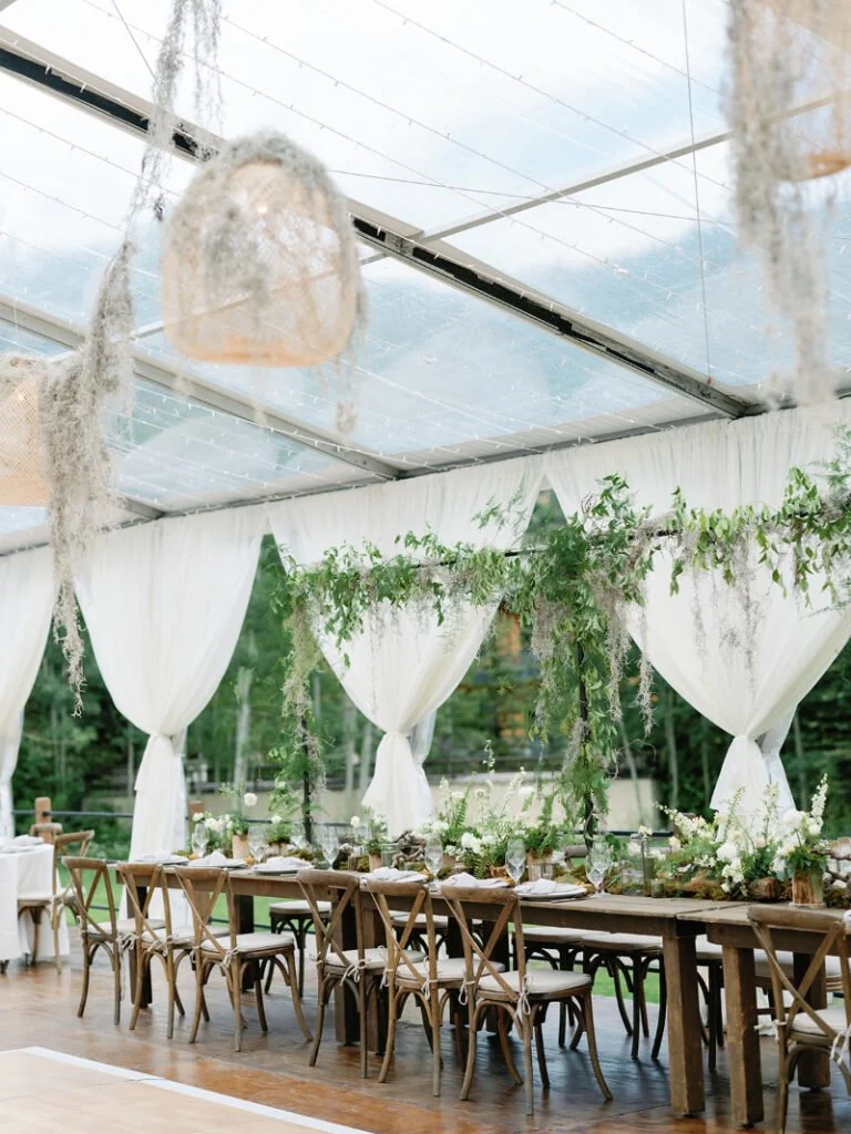 Wedding reception with draped tent, wood tables, and greenery reflecting elevated wedding design ideas.