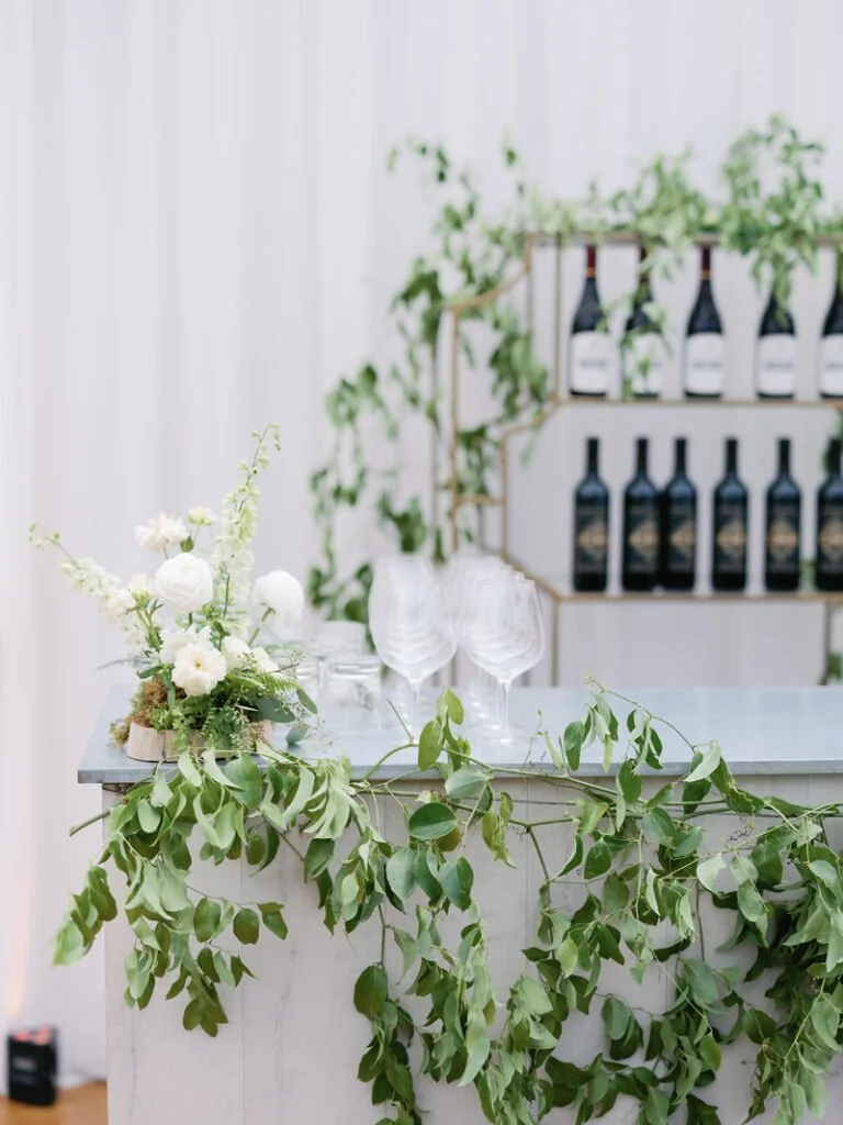 Wedding bar display with greenery garland, floral accents, and wine bottles for elevated wedding design ideas.
