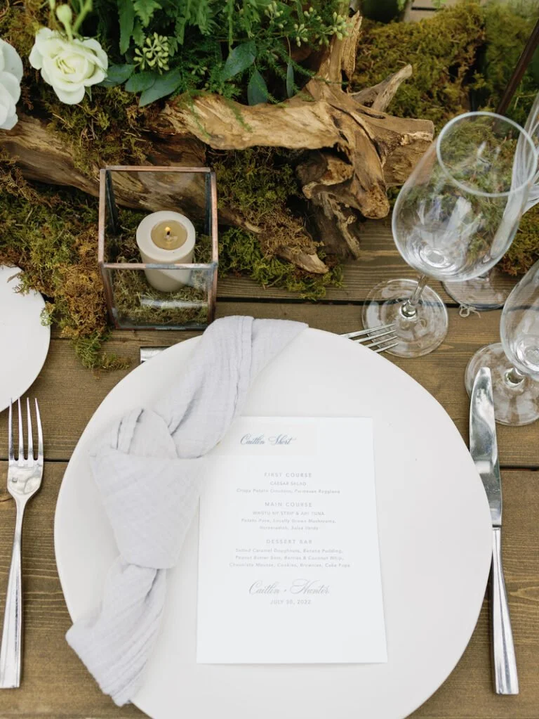 Close-up of wedding place setting with menu, knotted napkin, and mossy decor for refined wedding design ideas.