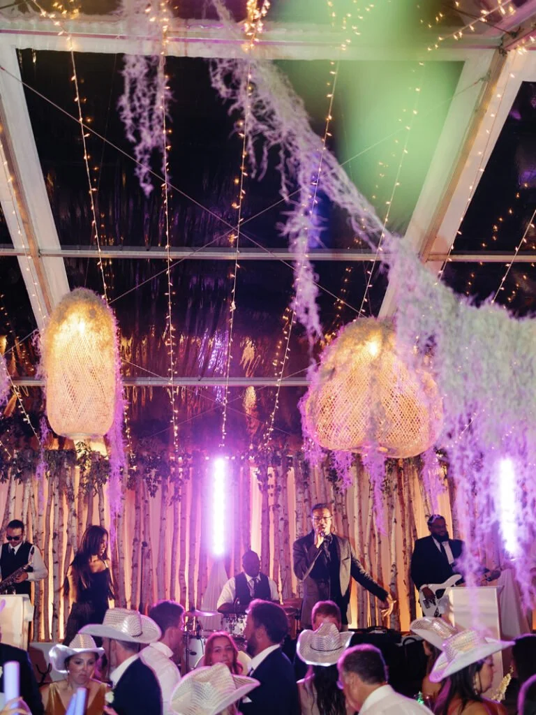 Live band on stage with birch backdrop and hanging rattan lights at an elegant Colorado wedding reception.