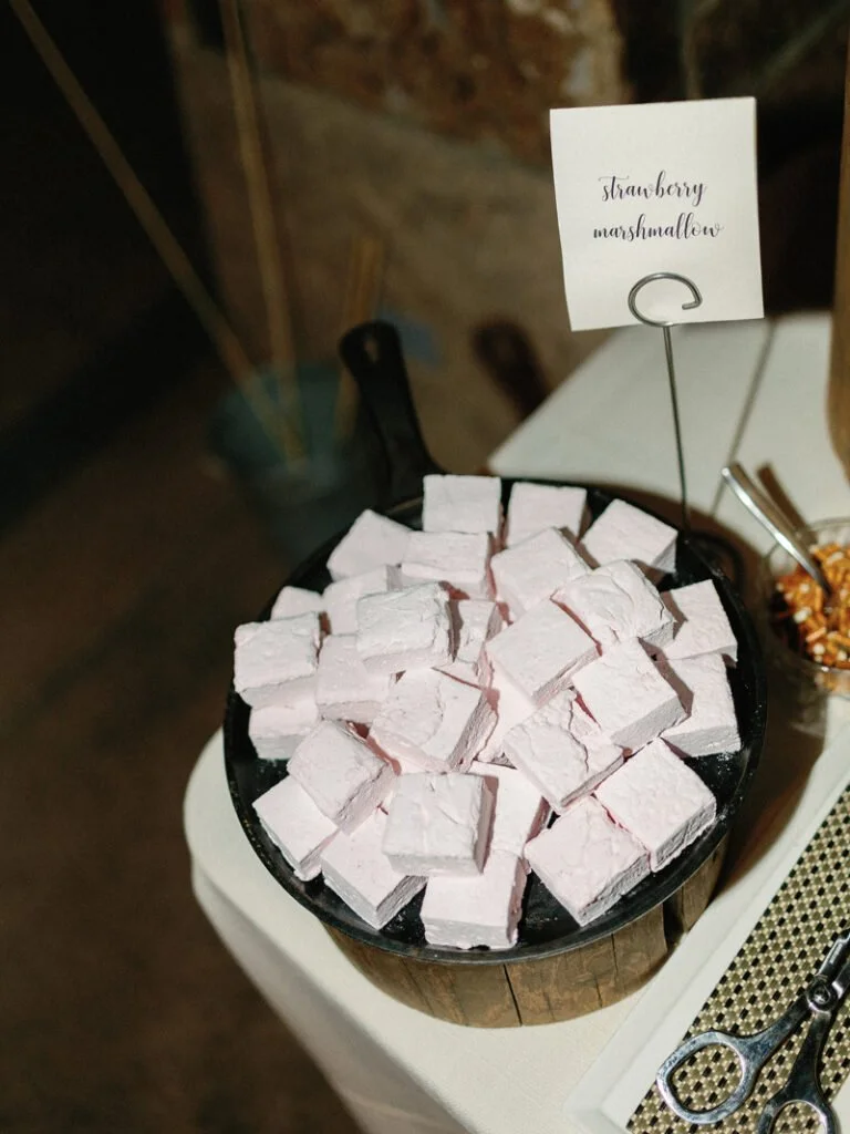 A bowl filled with pink strawberry marshmallows, placed on a wooden stand with a sign labeled "strawberry marshmallows."