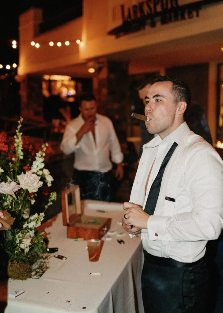 Groom in formalwear enjoying a cigar at the cigar bar during the wedding reception celebration.