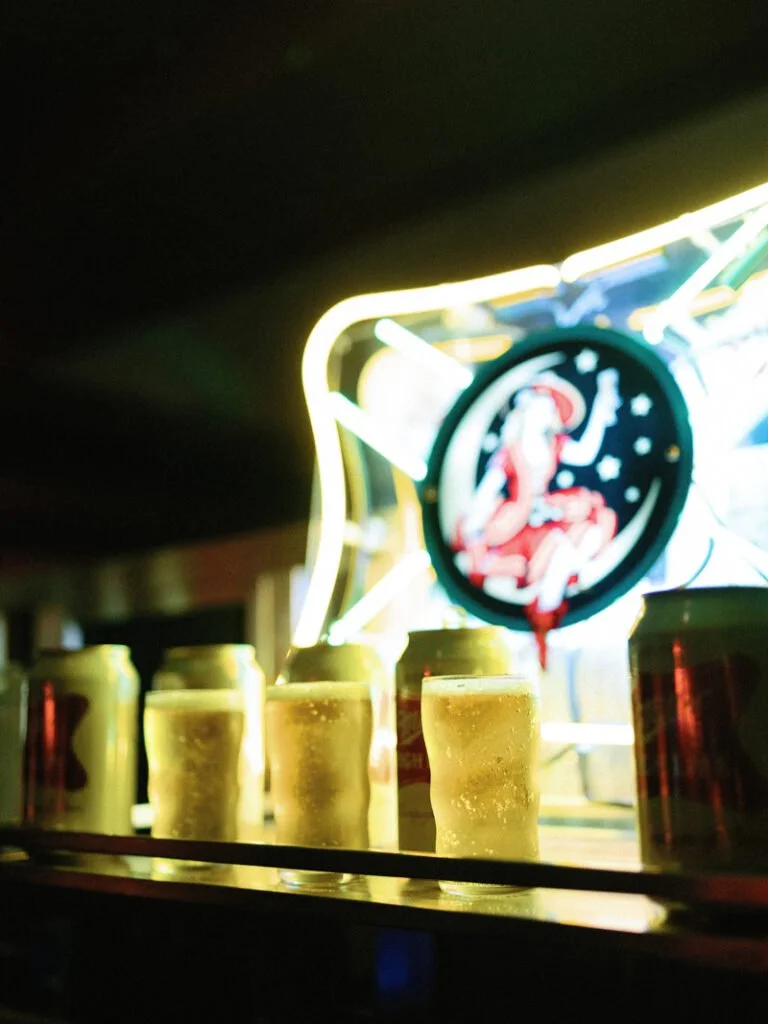 Close-up of cold beer cans and frosty mini glasses glowing under a retro neon wedding sign.