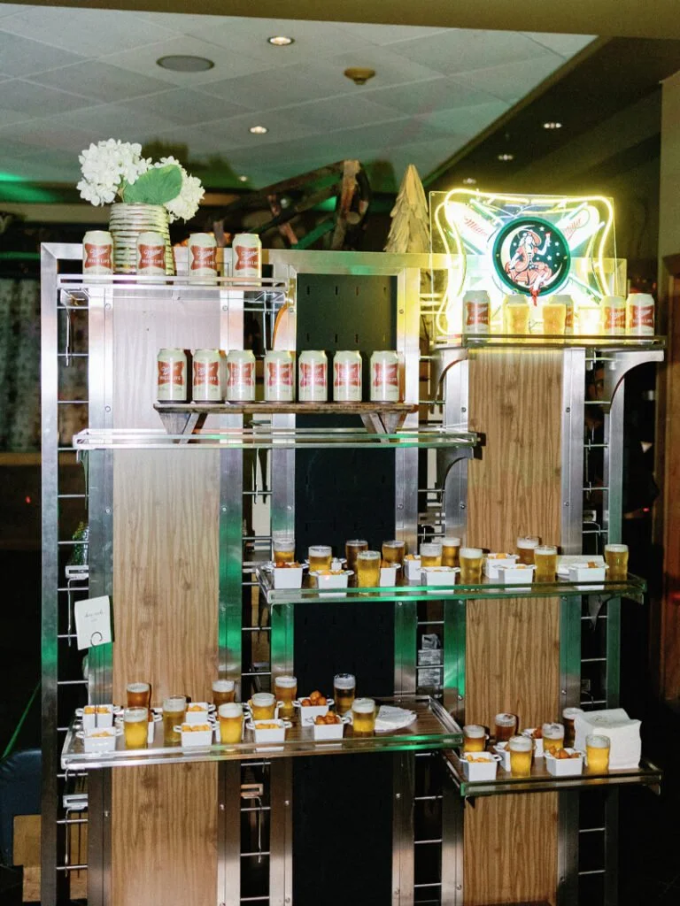 Modern wedding favor display with local honey jars, mini cans, and neon sign on metal shelving.