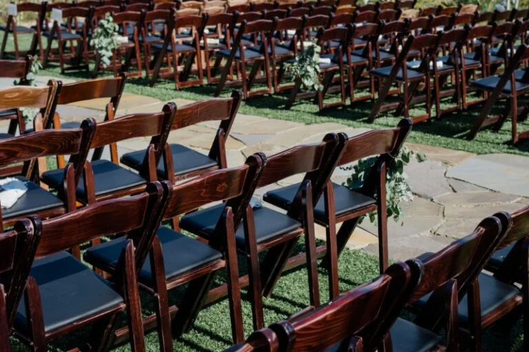 Rows of dark wood ceremony chairs with greenery accents, designed for a seamless wedding guest experience.