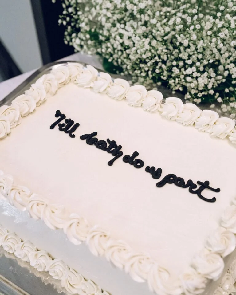 White wedding cake with scripted “Till death do us part,” ideal for romantic getaways in New England.