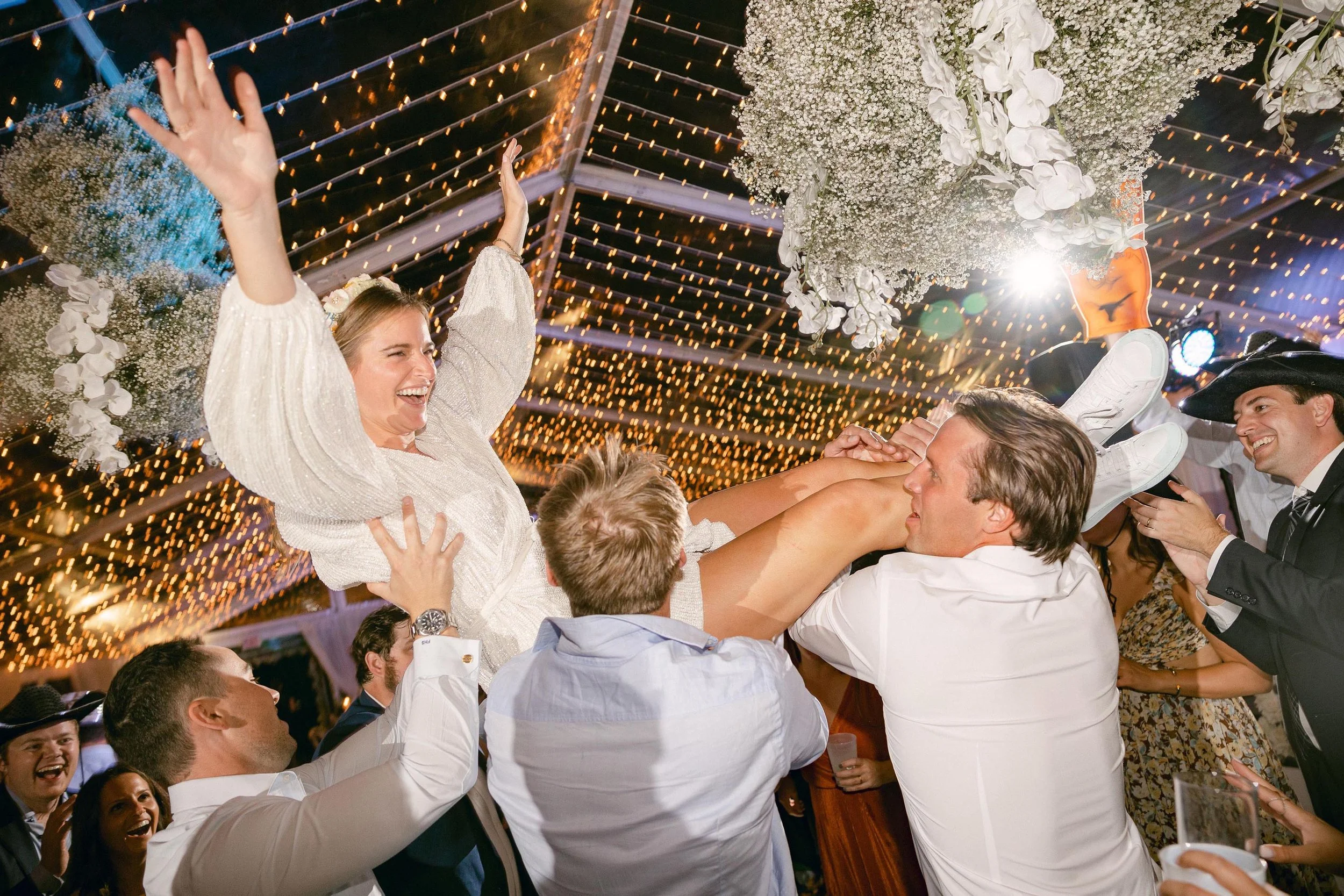 a bride getting lifted by friends and family at the party after her wedding