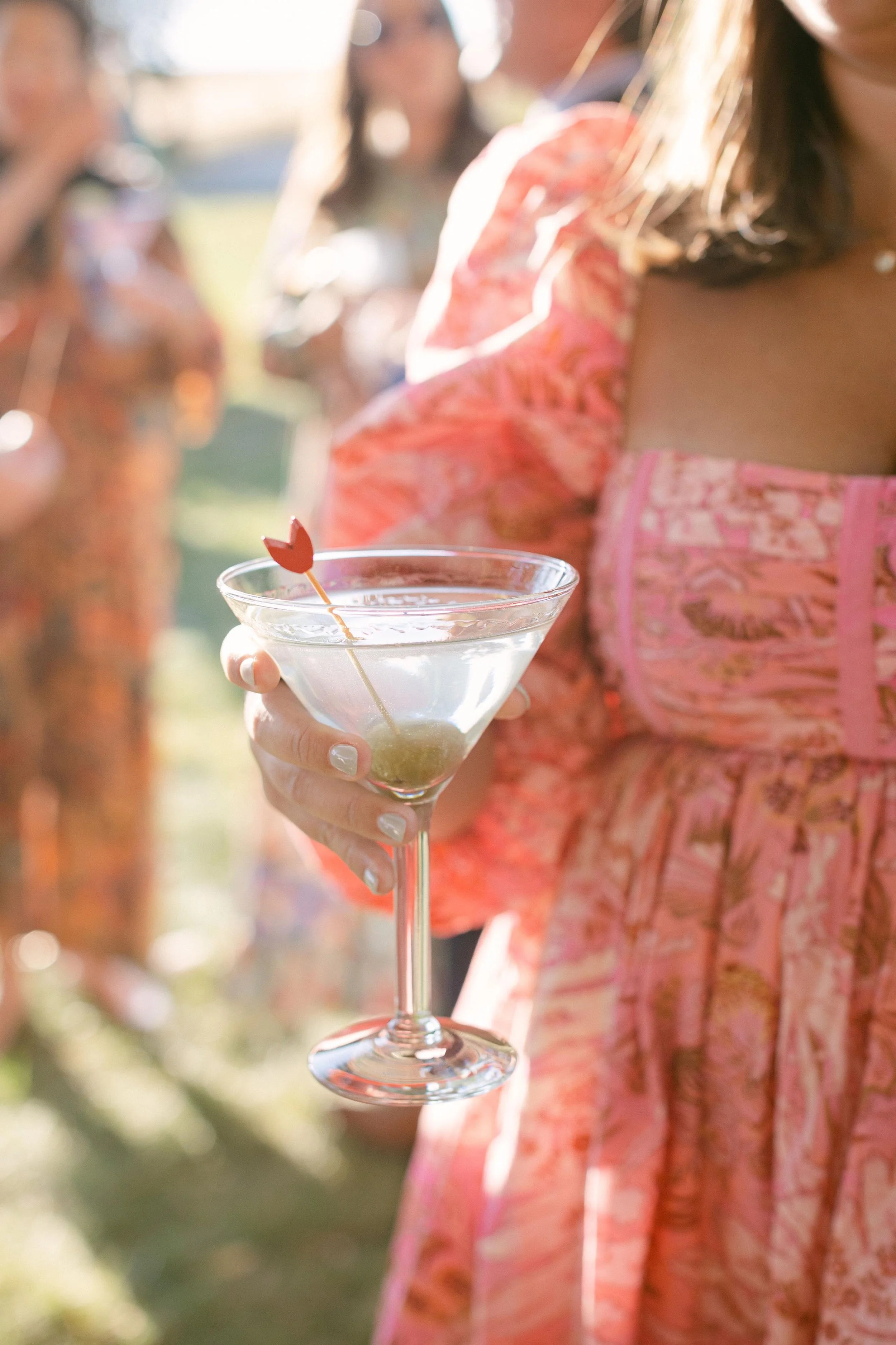 a cute martini drink held by a wedding guest wearing a colorful pink dress