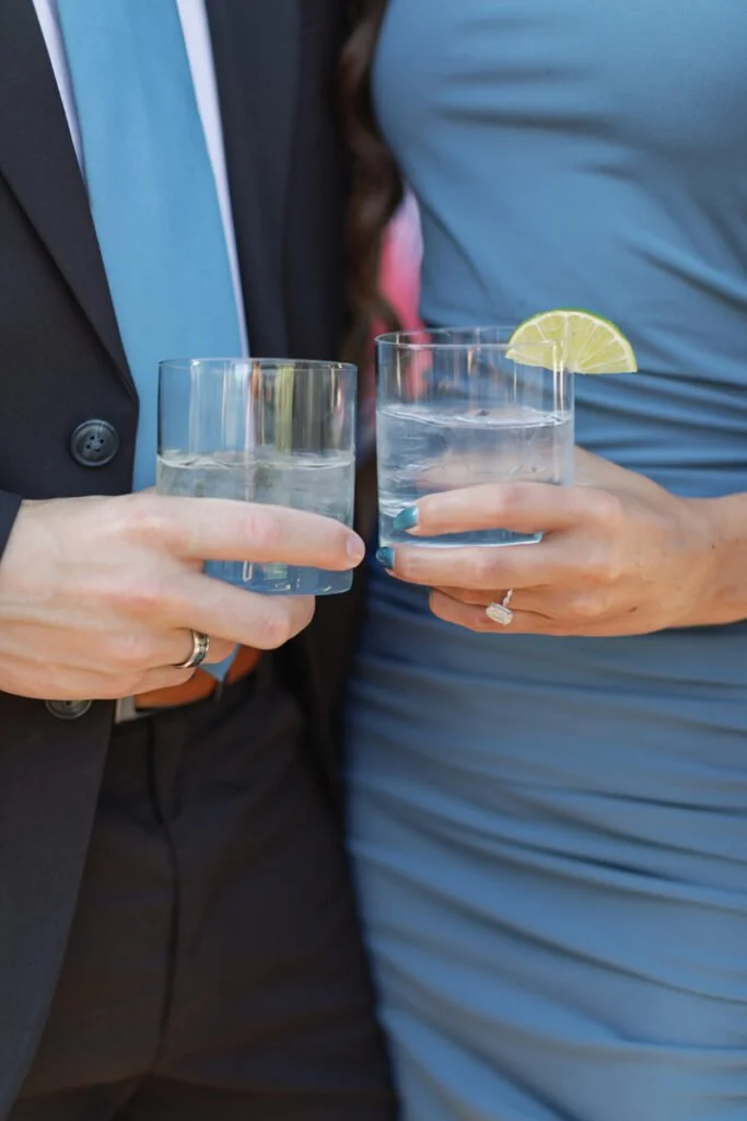 Couple toasting during multi-day wedding experiences, holding cocktails with lime while dressed in coordinated blue.