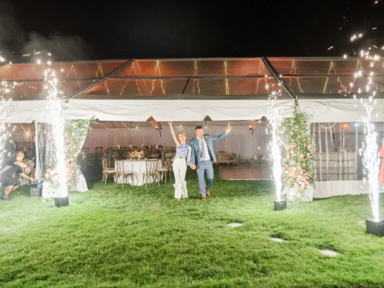 Couple makes a grand nighttime entrance under a tent with cold sparklers and floral installations.