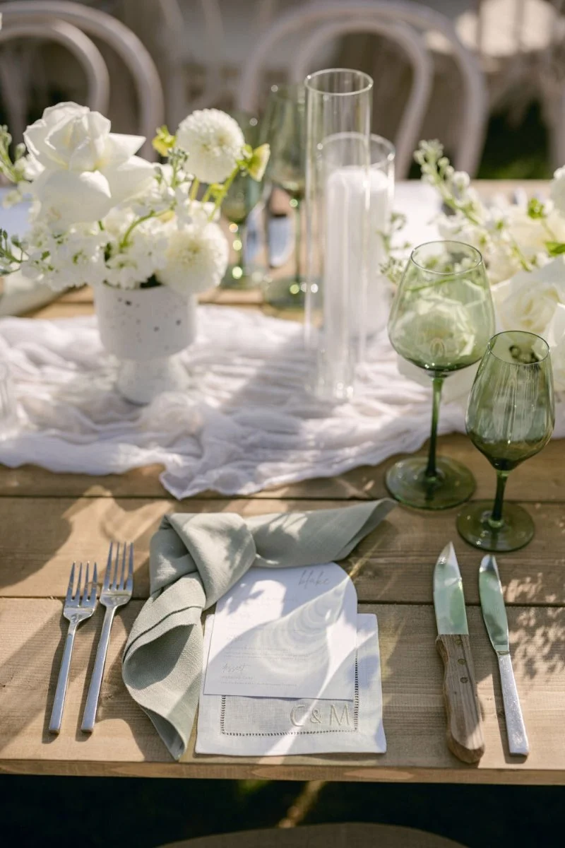 Elegant wedding place setting with sage green napkin, personalized menu, silver cutlery, and green glassware.