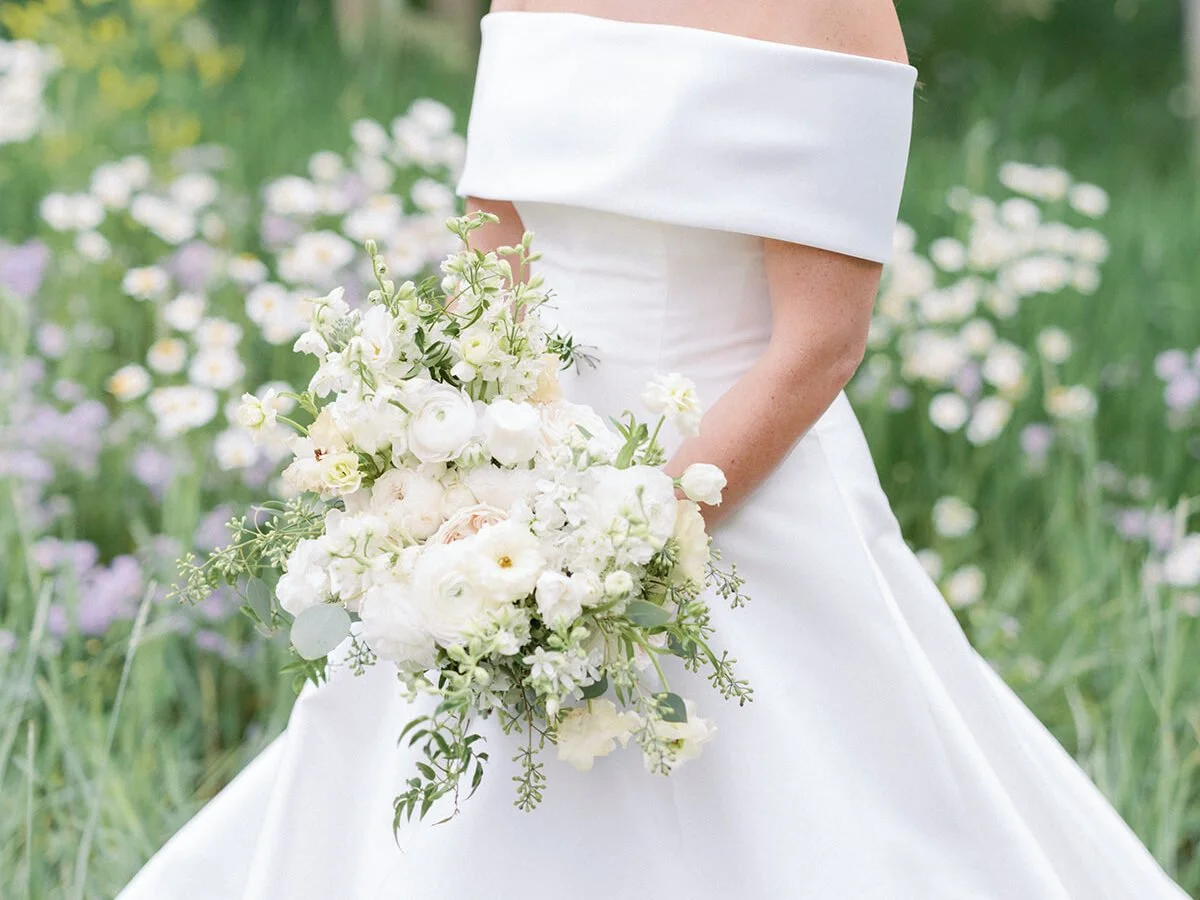 Bride holding white bouquet in wildflower meadow, showcasing timeless and elegant wedding design ideas.